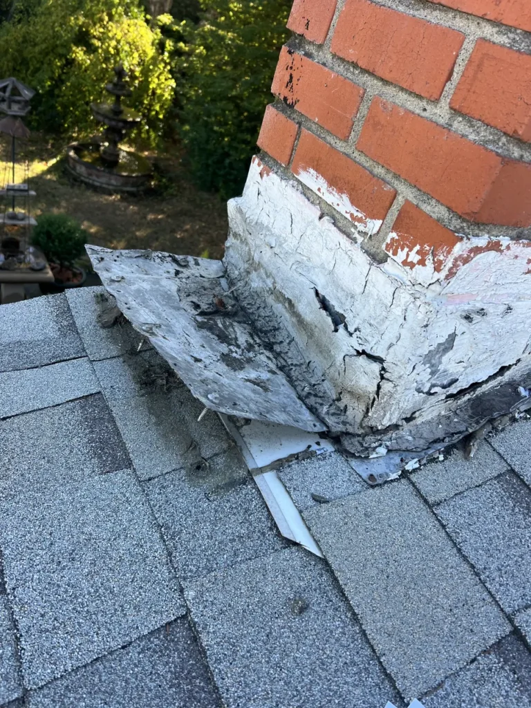 Cracked patching and worn flashing at the base of a brick chimney before repair