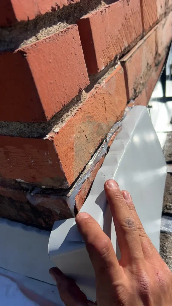 Fitting new metal flashing against the brick chimney during the repair